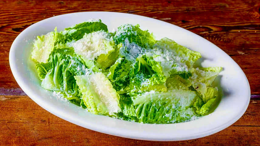 Plate of fresh romaine lettuce leaves topped with grated Parmesan cheese, served on a white oval dish